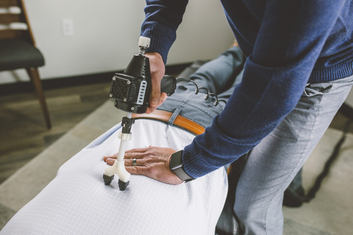 Chiropractor performing a gentle instrument adjustment on a patient's spine using a handheld adjusting tool